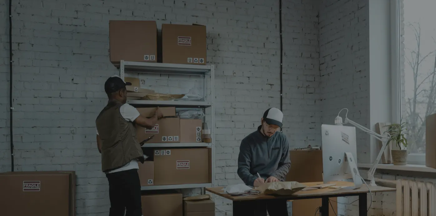 Two workers packaging products into shipping boxes at an ecommerce fulfillment workspace.